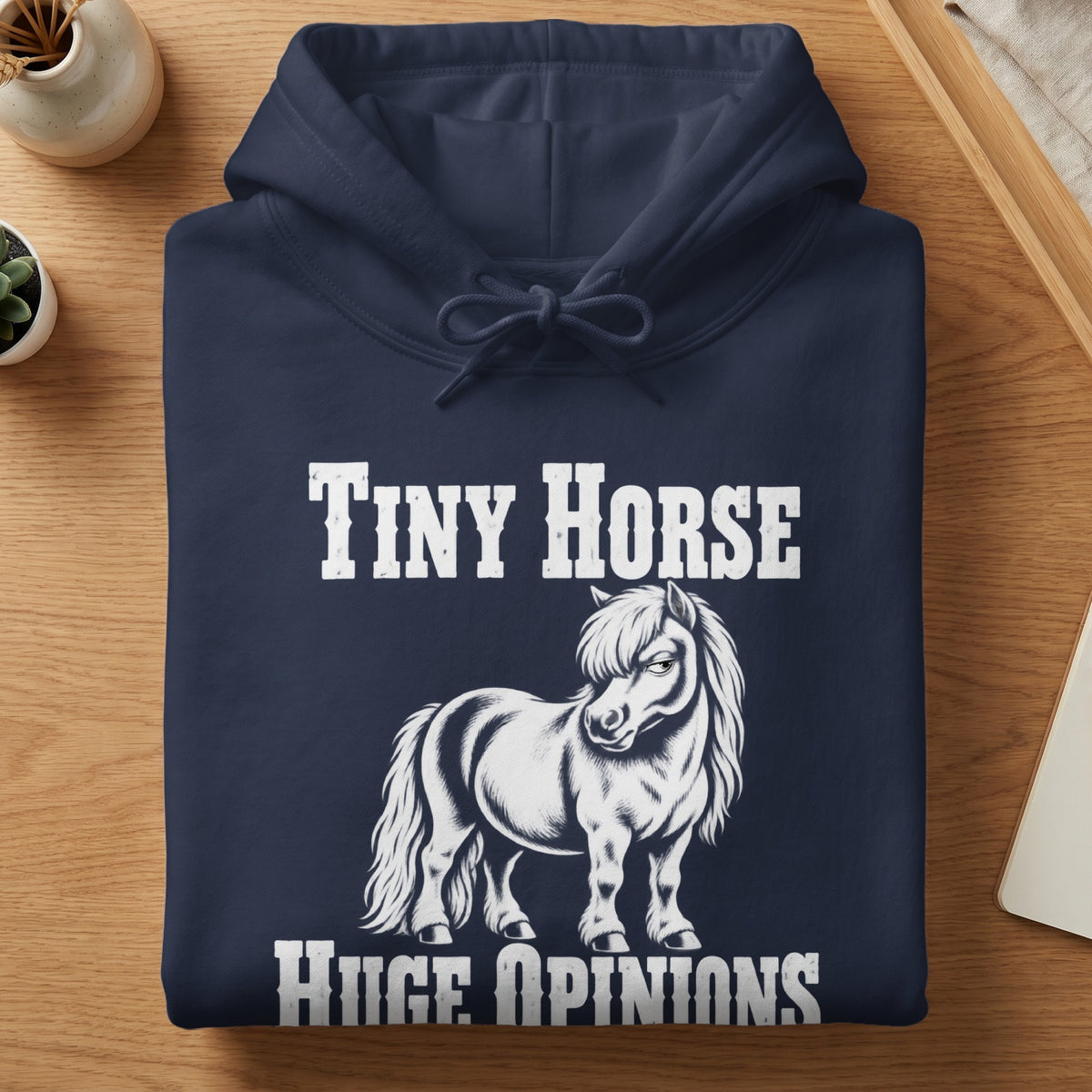 A folded dark blue hoodie featuring the white text Tiny Horse Huge Opinions and a graphic of a small, stern-looking pony.