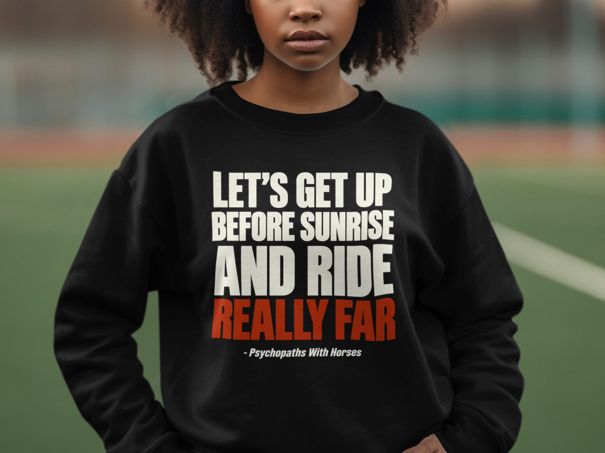 A person wearing a black sweatshirt with white and red text reading "Let's Get Up Before Sunrise and Ride Really Far - Psychopaths With Horses".