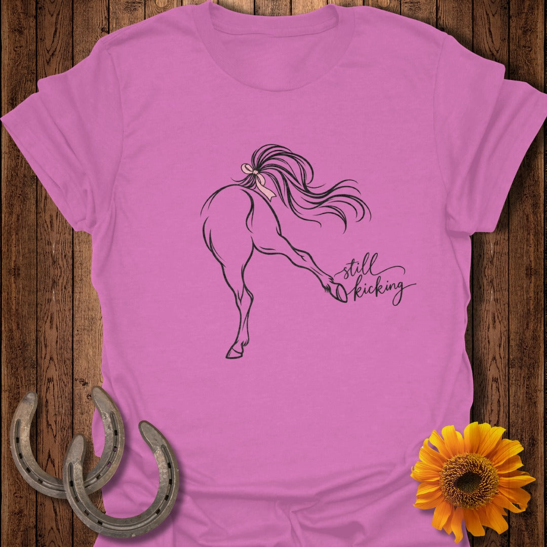 Pink t-shirt with a line drawing of a horse kicking and the text "still kicking".