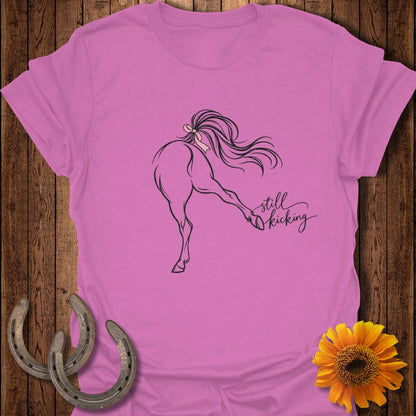 Pink t-shirt with a line drawing of a horse kicking and the text "still kicking".