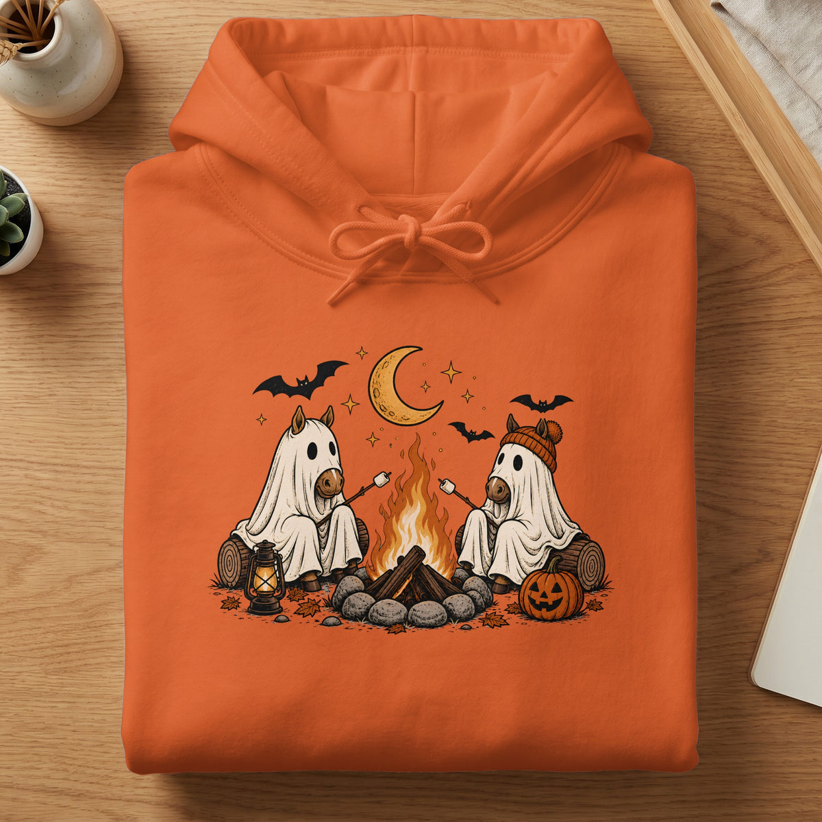 Two horses in ghost costumes roast marshmallows by a campfire under a crescent moon.