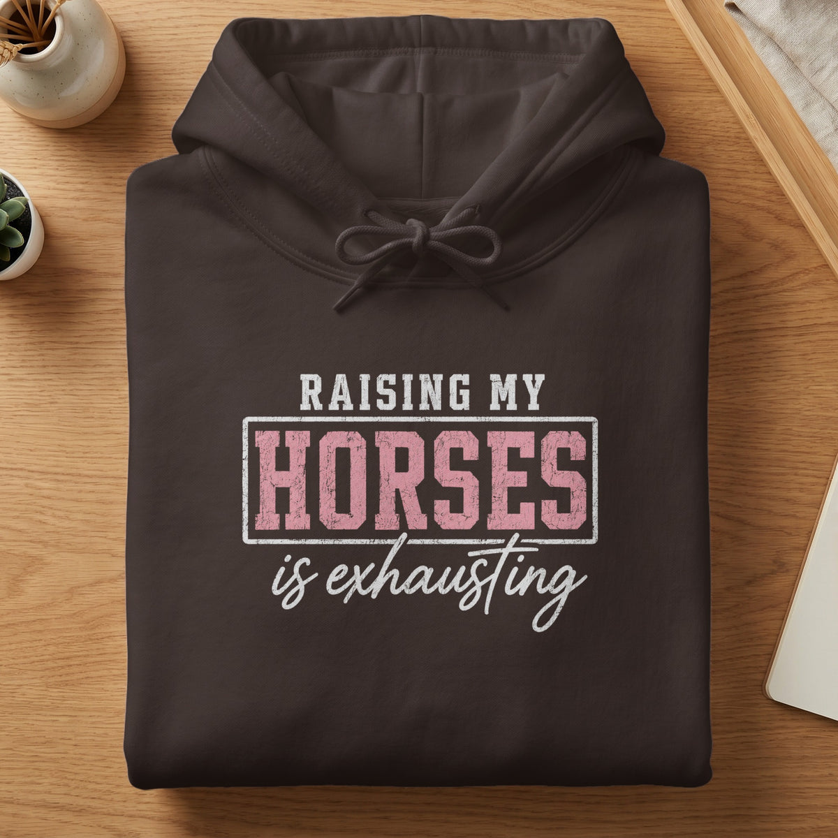 Dark brown hoodie with white and pink text that reads "RAISING MY HORSES is exhausting."