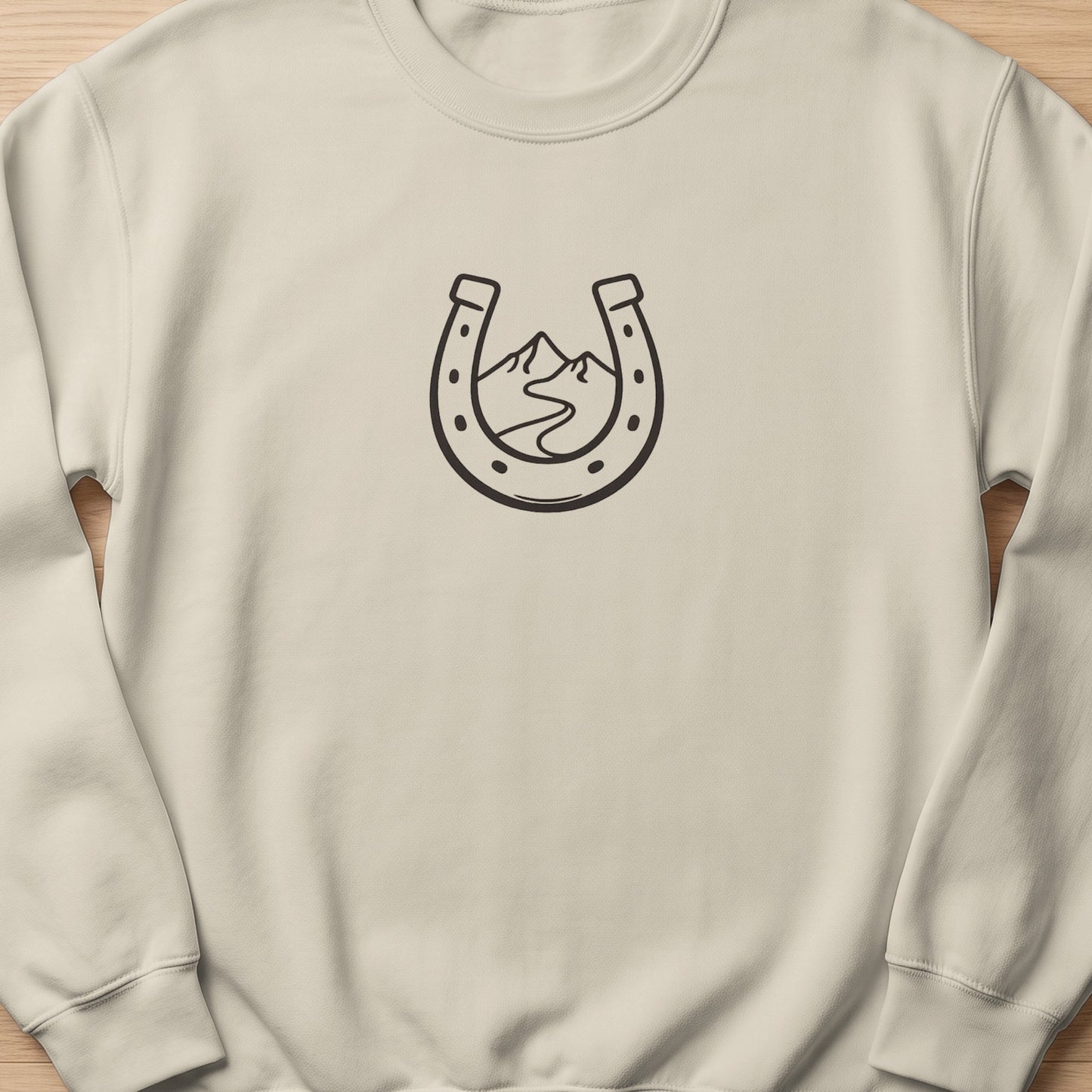 Cream sweatshirt with a black line art horseshoe and mountain landscape design.