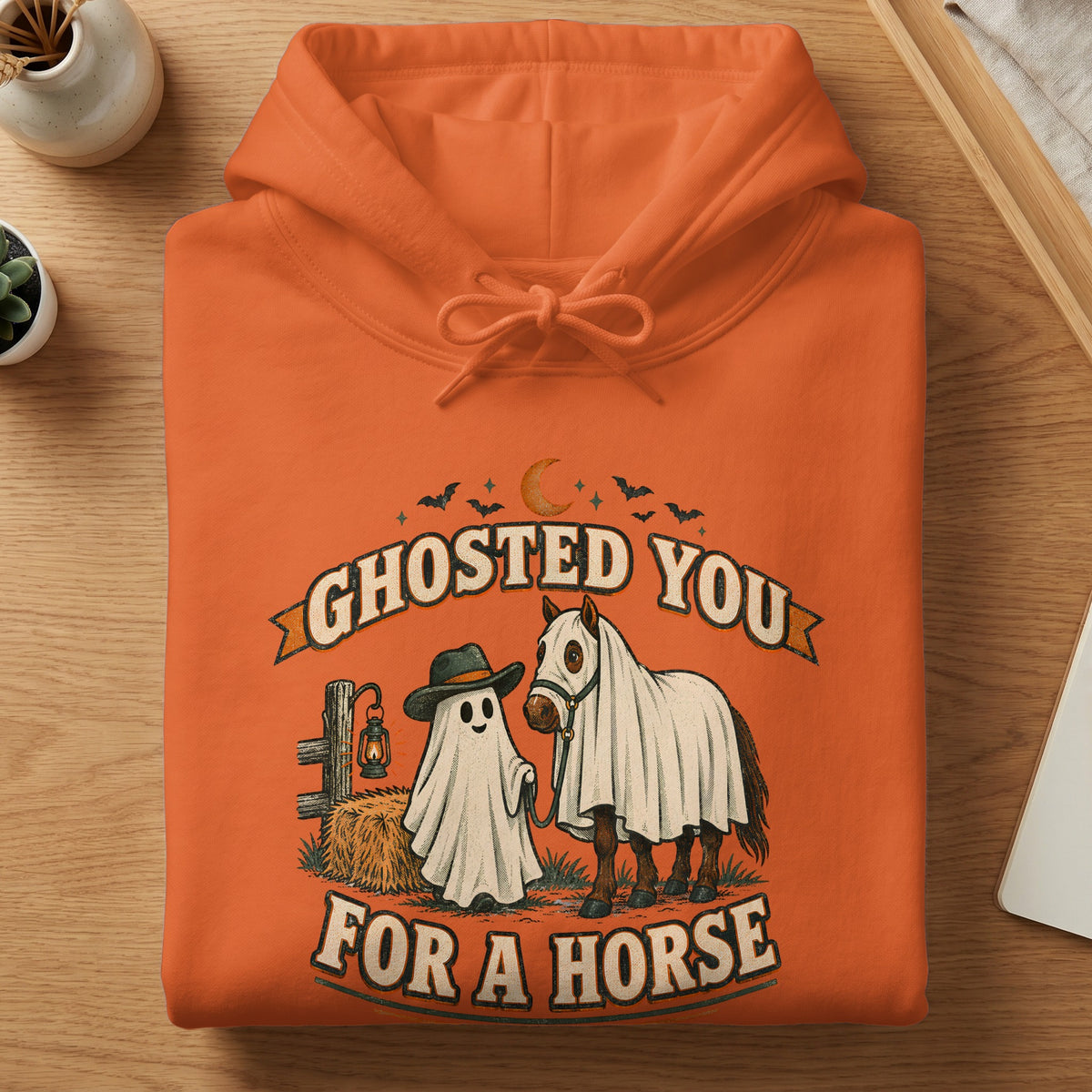Orange hoodie with a ghost, horse, and fence graphic that says "Ghosted You For A Horse".