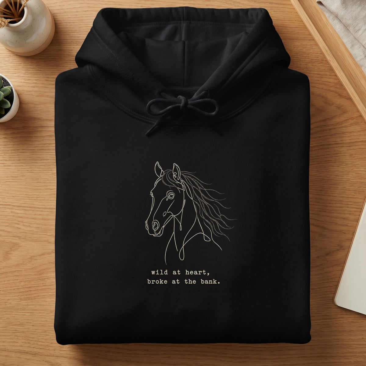 Black hoodie with line art horse and text "wild at heart, broke at the bank."
