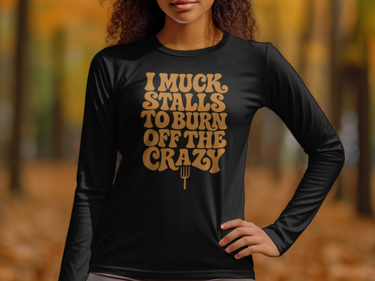 Black long-sleeve shirt with gold text "I muck stalls to burn off the crazy".