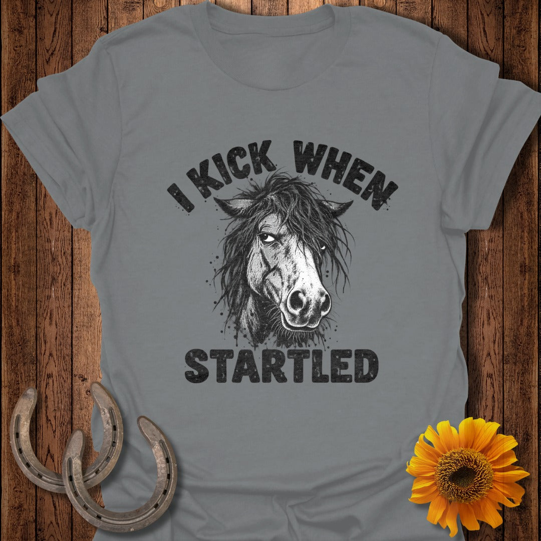 Gray t-shirt featuring a horse graphic with the text I KICK WHEN STARTLED, alongside horseshoes and a sunflower.