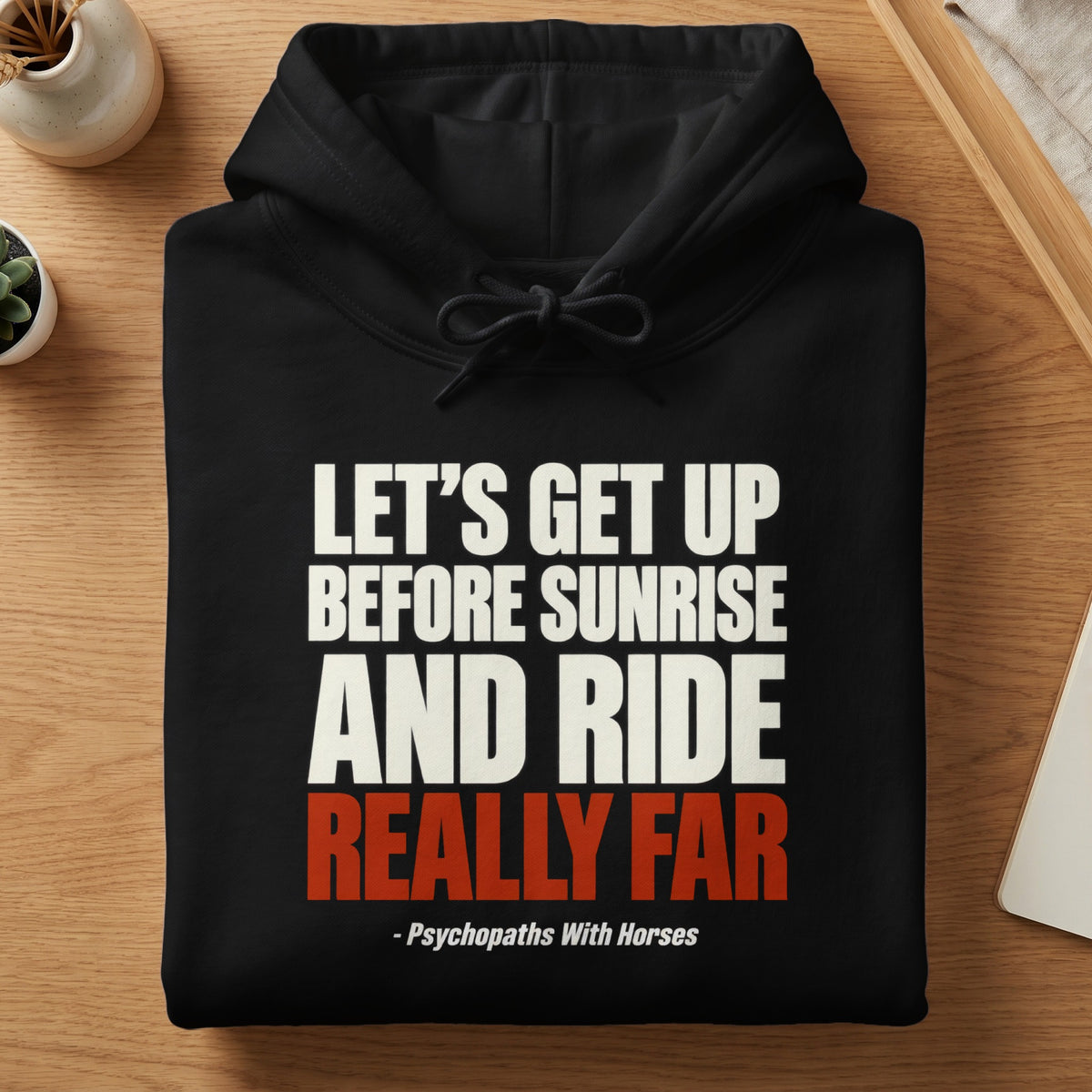 A folded black hooded sweatshirt featuring white and red text that reads Let us get up before sunrise and ride really far - Psychopaths With Horses.