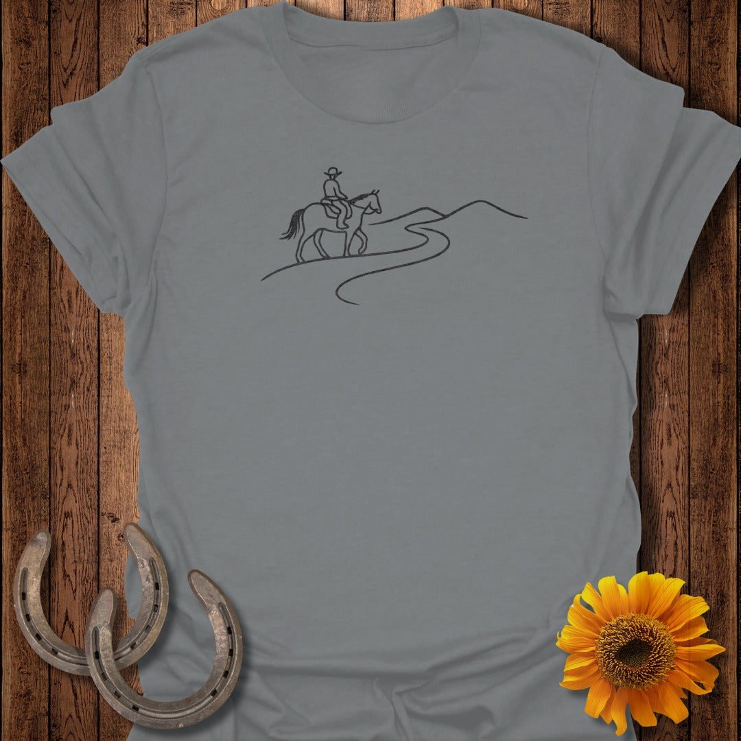 Grey t-shirt graphic of a cowboy riding a horse along a winding road.