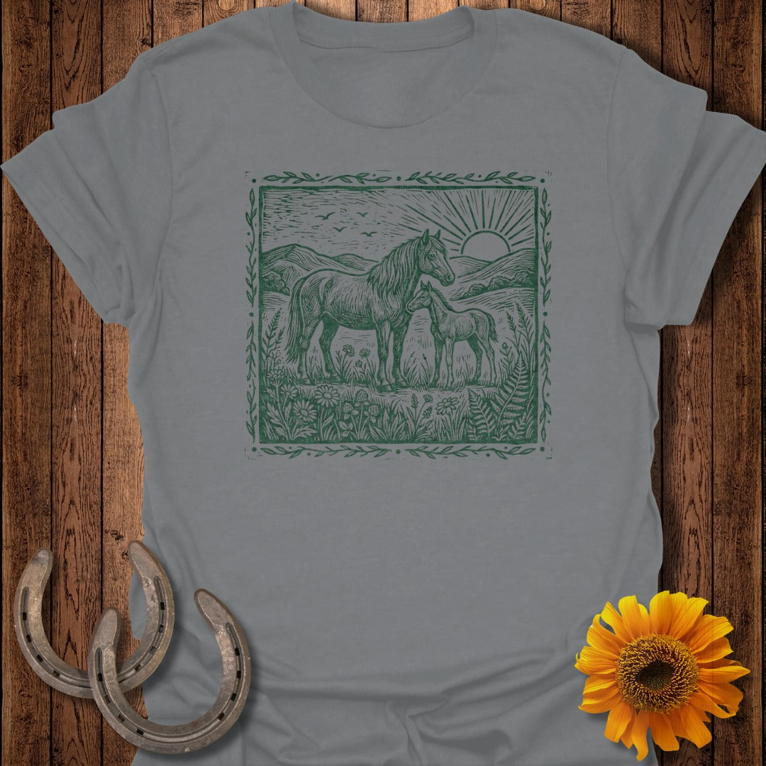 Grey t-shirt with a green linocut design of horses and sun in a meadow.