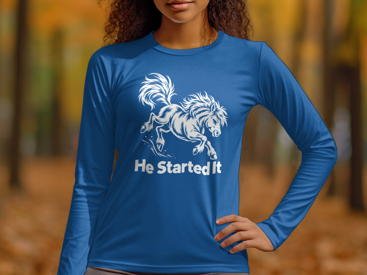 A person wears a blue long-sleeved shirt with a white graphic of a galloping horse and the text He Started It.