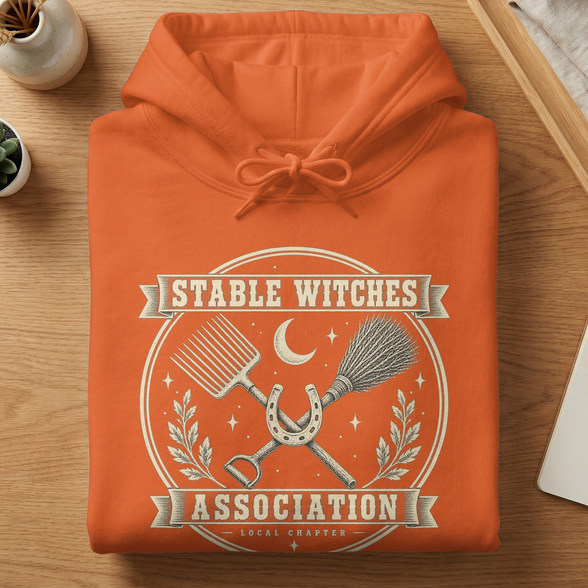 Orange hoodie with "Stable Witches Association" text and farm tool graphics.