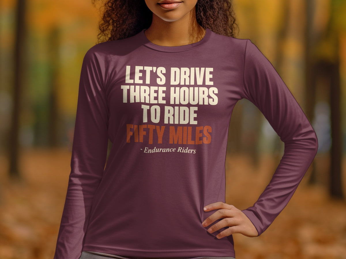 A woman wearing a maroon long-sleeve shirt with text reading Let's Drive Three Hours To Ride Fifty Miles.