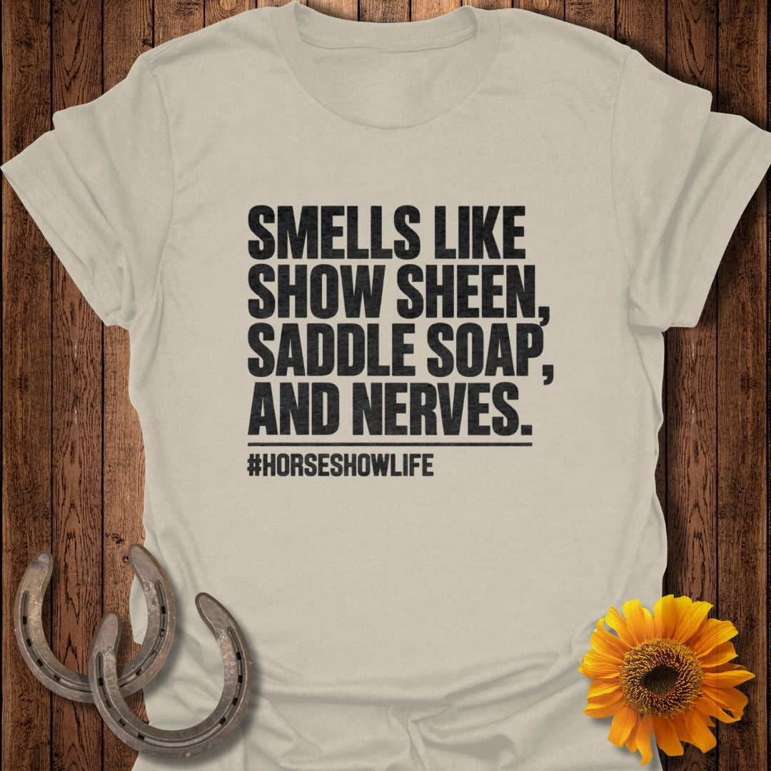 A cream t-shirt printed with black text reading SMELLS LIKE SHOW SHEEN, SADDLE SOAP, AND NERVES.