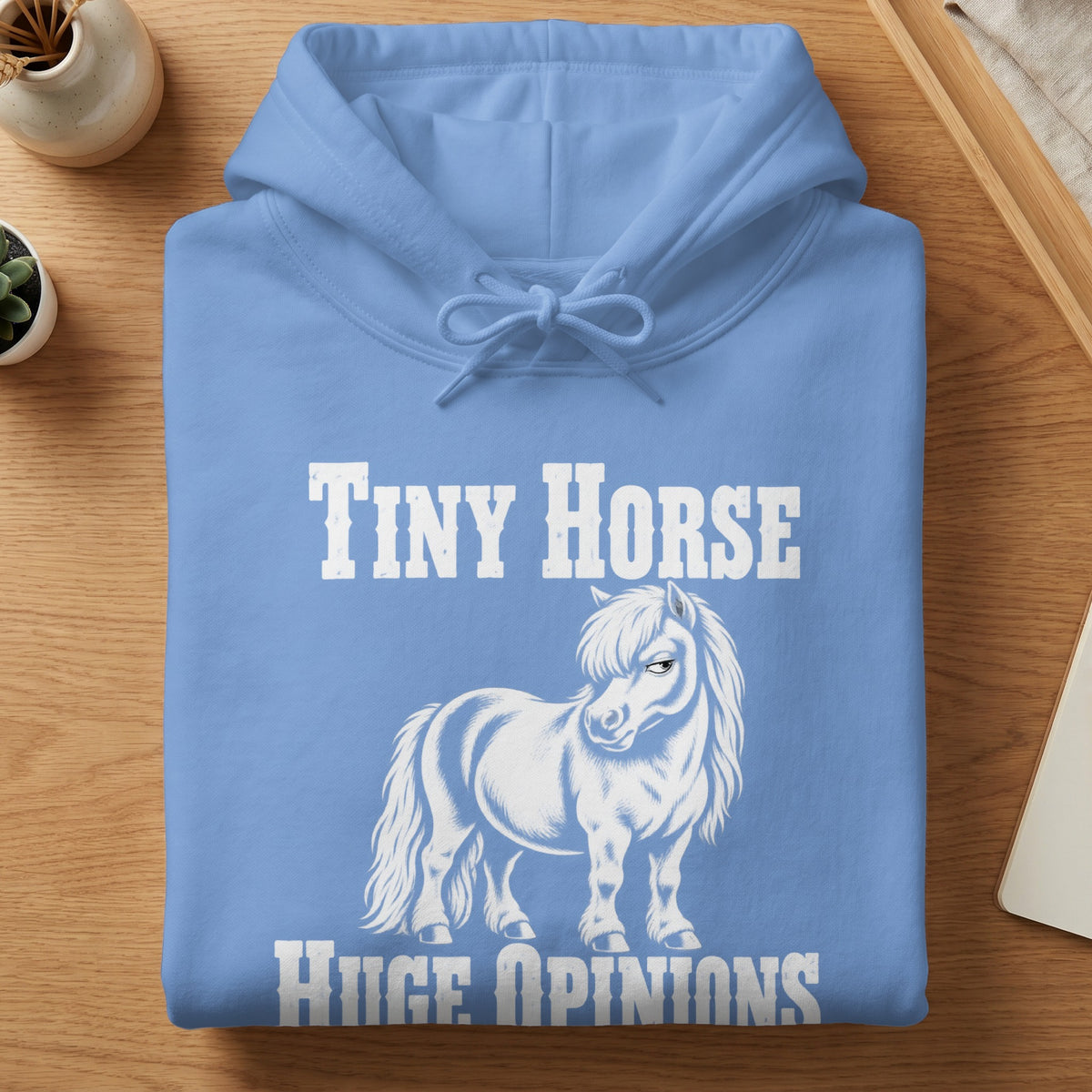 A light blue hoodie with white text that reads Tiny Horse Huge Opinions above and below a graphic of a sarcastic-looking pony.