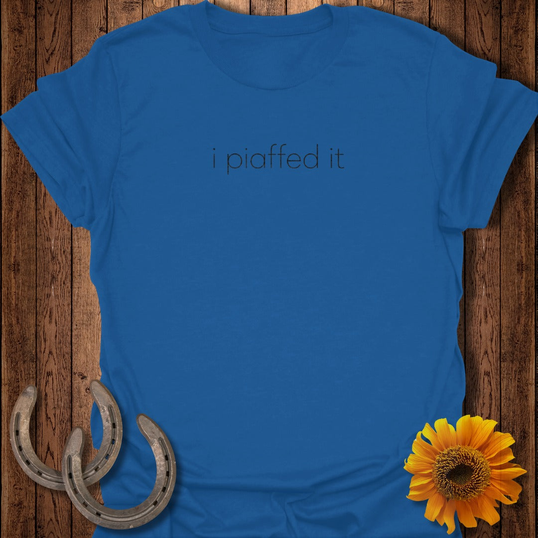 Blue t-shirt with "i piaffed it" text, on wooden background with horseshoes and sunflower.
