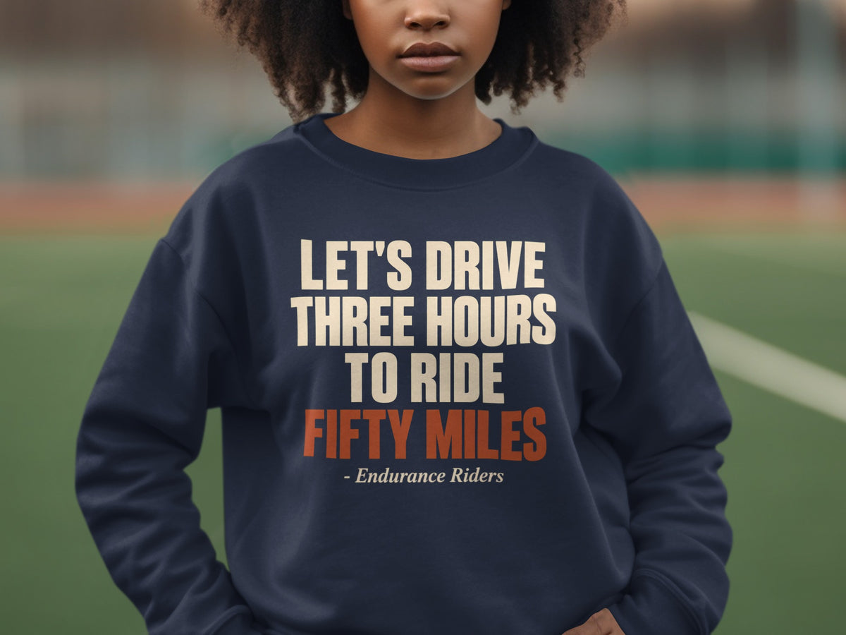 A person wearing a dark blue crewneck sweatshirt with the text "LET'S DRIVE THREE HOURS TO RIDE FIFTY MILES - Endurance Riders" printed on the chest.