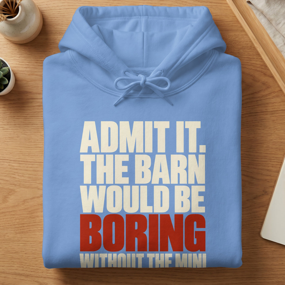 Light blue hoodie with white and red text stating ADMIT IT THE BARN WOULD BE BORING WITHOUT THE MINI folded on a wooden table.