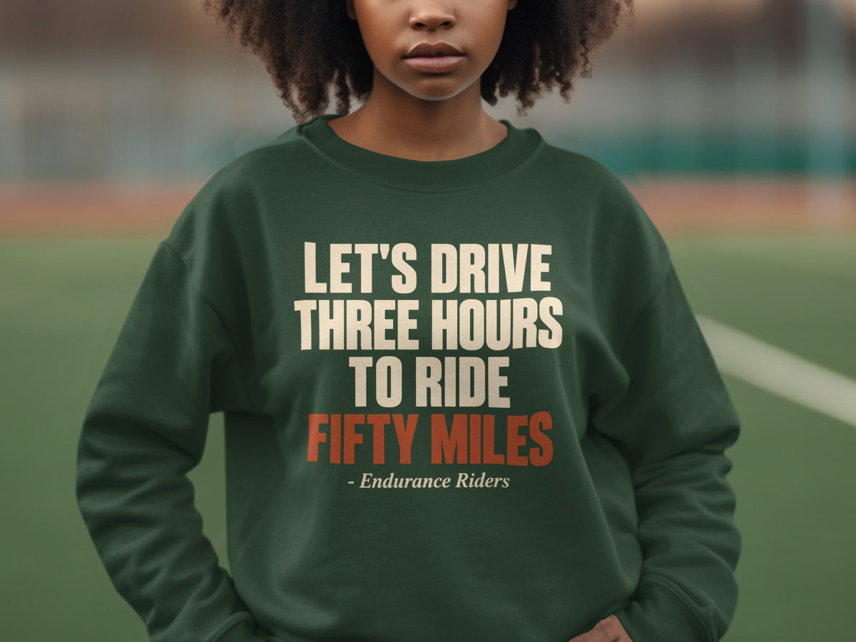 A person wearing a dark green crewneck sweatshirt featuring the text Let's Drive Three Hours To Ride Fifty Miles.