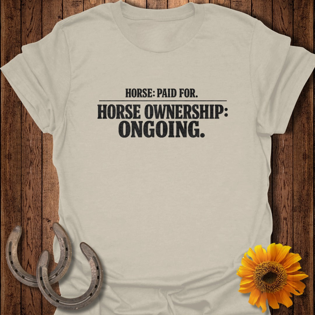 Light beige t-shirt with "Horse: Paid For. Horse Ownership: Ongoing." text and decorative horseshoes and sunflower.