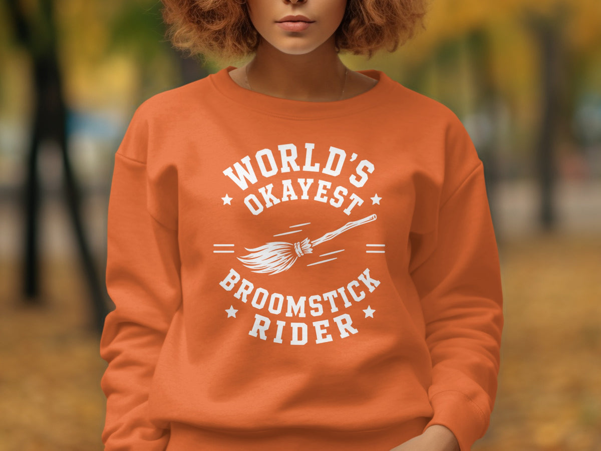 Orange sweatshirt with "World's Okayest Broomstick Rider" graphic and broom illustration.
