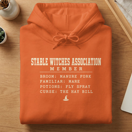 Orange hoodie with "Stable Witches Association Member" text and witch hat graphic.