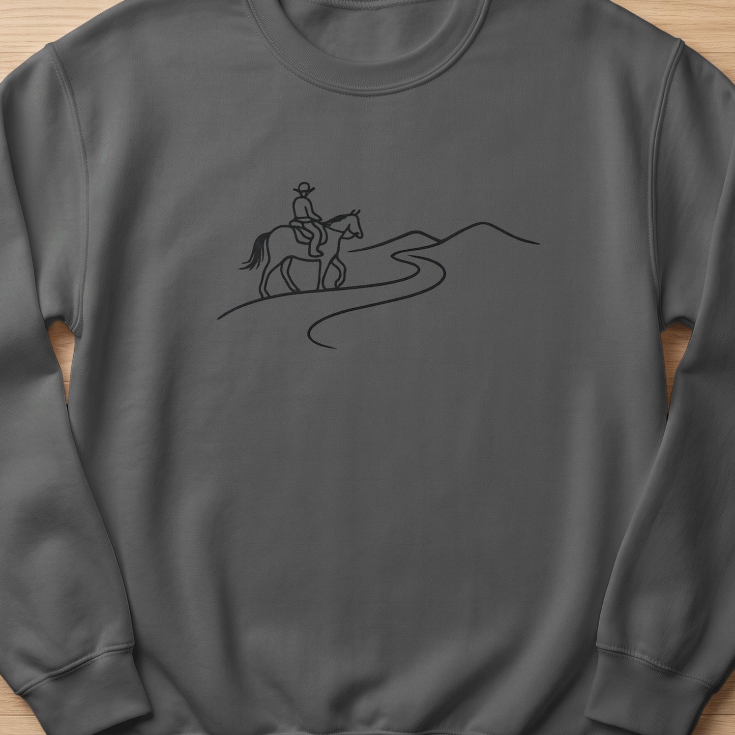Line art of a cowboy on horseback riding on a winding path through hills.