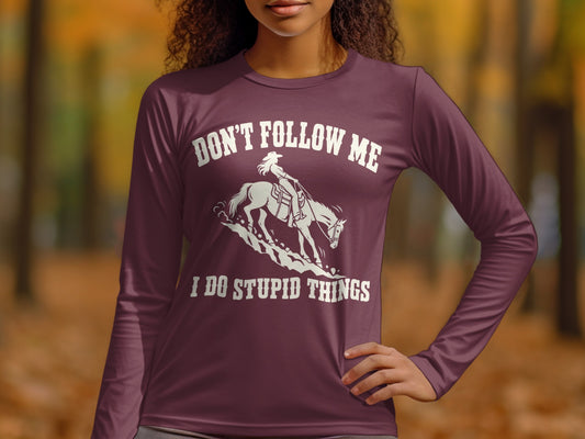 A woman wearing a dark red long-sleeve shirt with a white graphic of a horse and rider and the text "DON'T FOLLOW ME I DO STUPID THINGS."