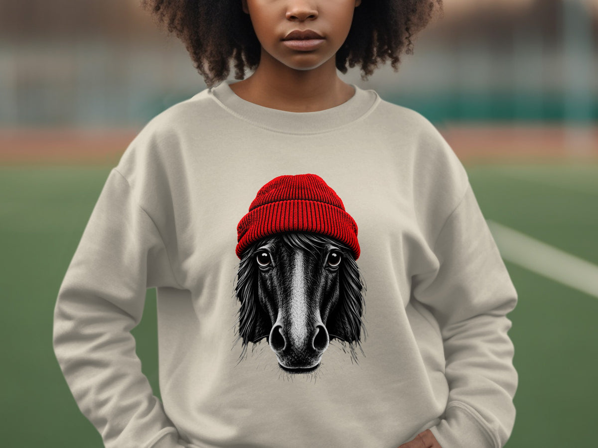 A person wearing a beige crewneck sweatshirt printed with a black-and-white horse wearing a red beanie.