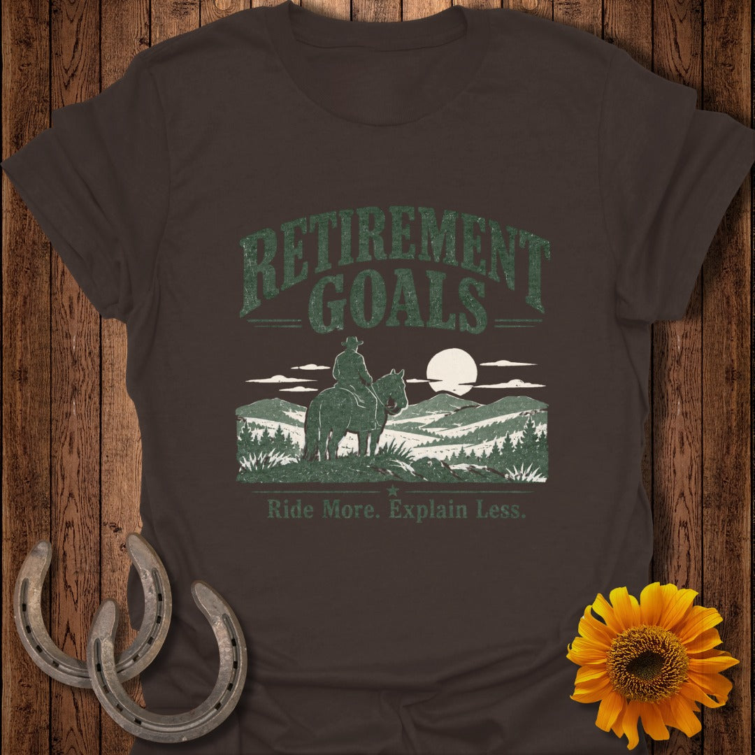 Brown t-shirt with "Retirement Goals" graphic, a cowboy on a horse in mountains, and "Ride More. Explain Less."