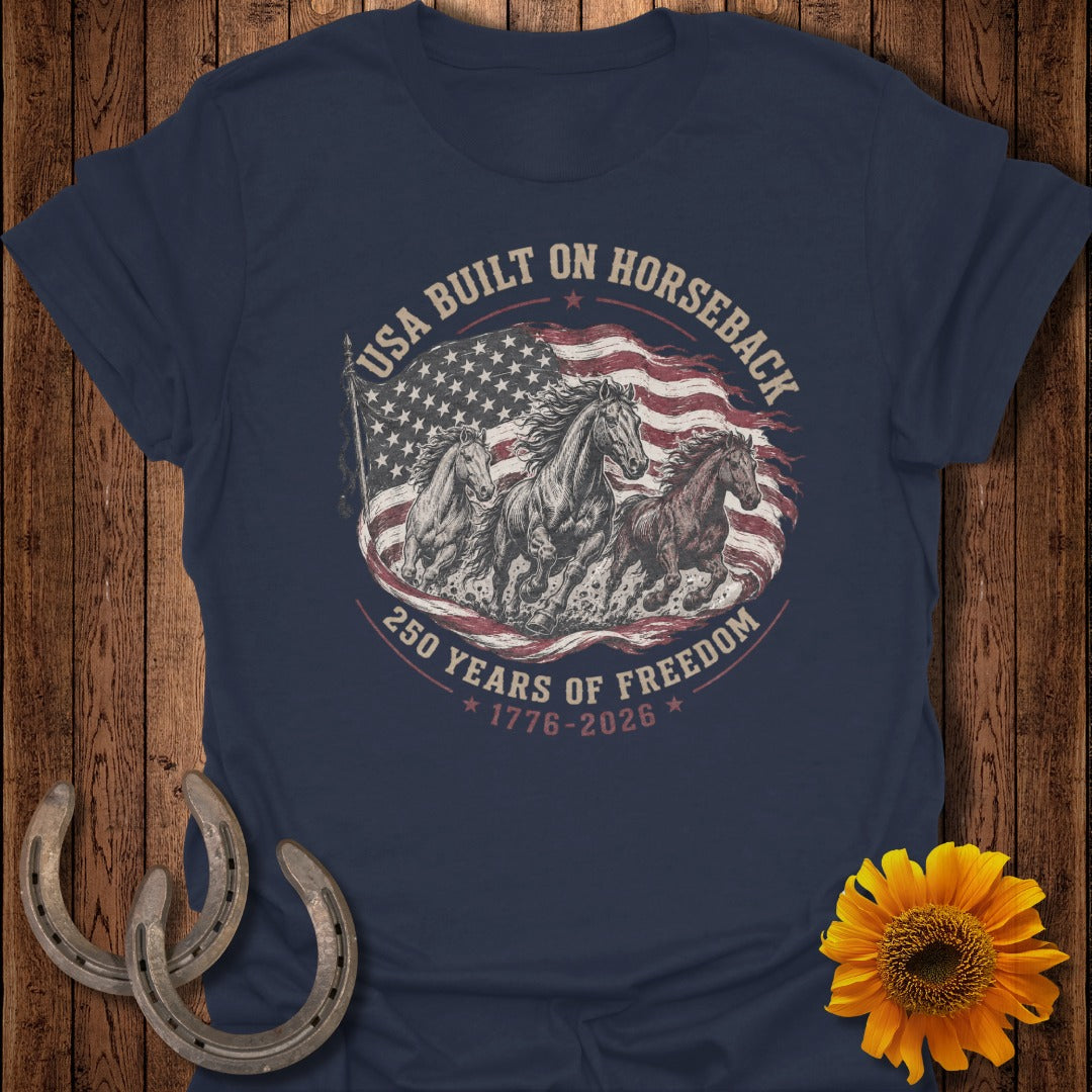 Navy t-shirt with horses running in front of the American flag and text "USA BUILT ON HORSEBACK 250 YEARS OF FREEDOM 1776-2026".