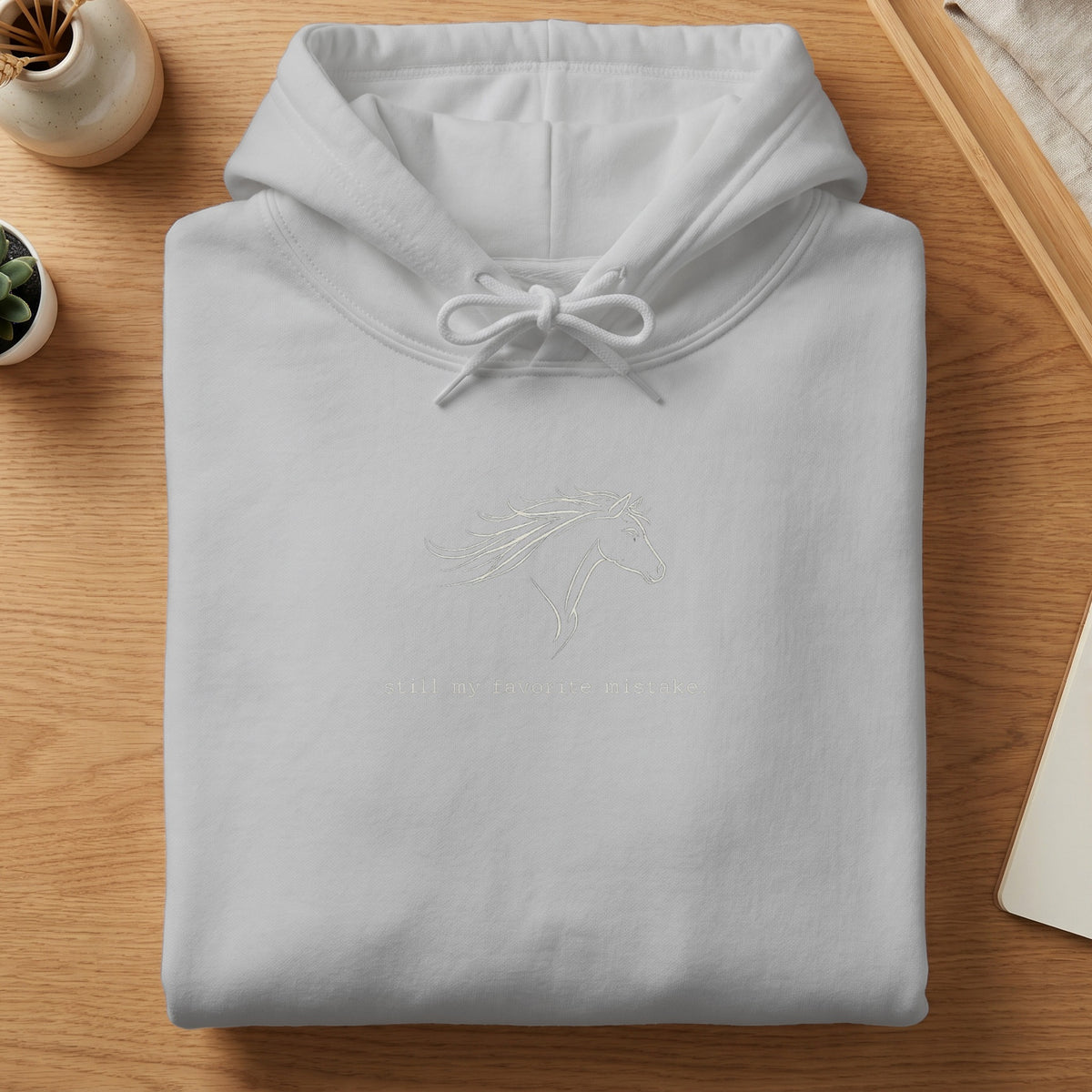 White hoodie with a line art horse graphic and text "still my favorite mistake."