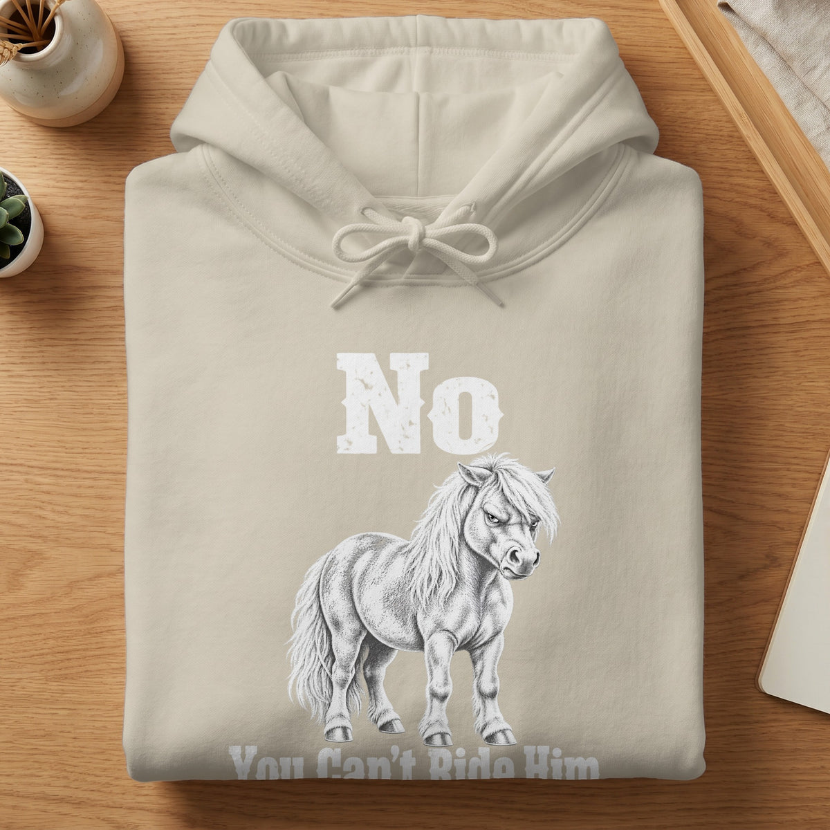 A folded beige hoodie featuring a sketched illustration of an angry pony with the text No You Cant Ride Him.