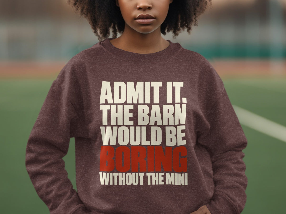 A person wearing a brown crewneck sweatshirt printed with the text ADMIT IT. THE BARN WOULD BE BORING WITHOUT THE MINI.