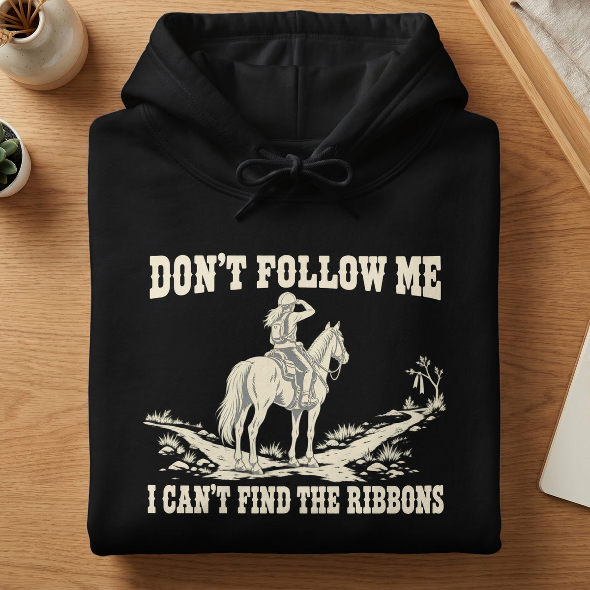 A folded black hoodie with an equestrian graphic and the text Don't follow me I can't find the ribbons.
