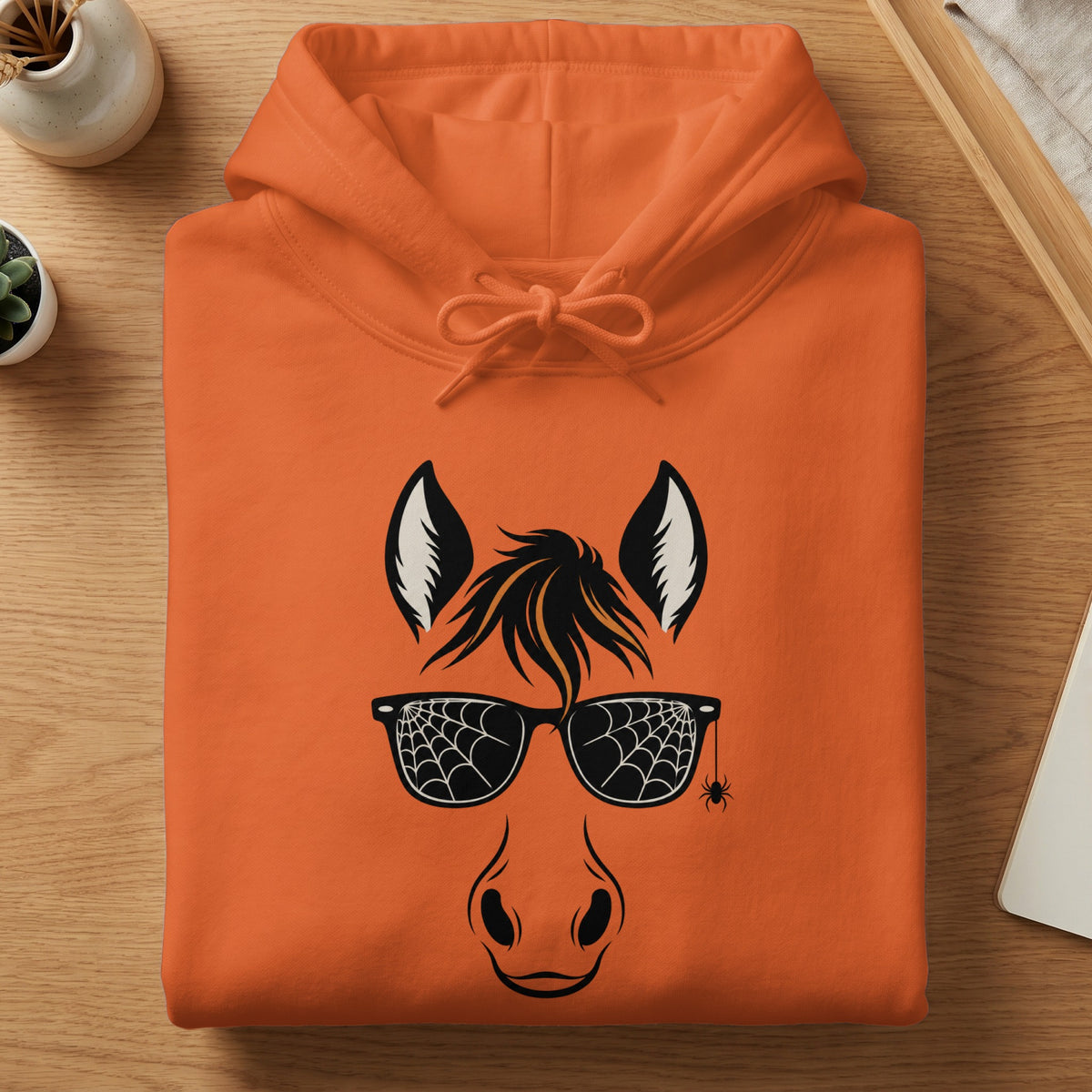 Orange hoodie with a black horse face graphic wearing spiderweb sunglasses.