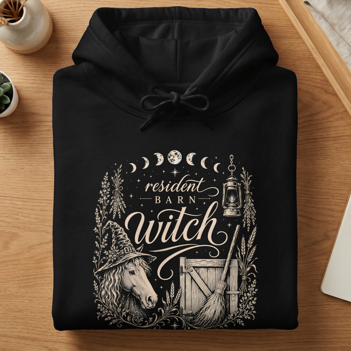 Black hoodie with "resident barn witch" design featuring horse, broom, and moon phases.