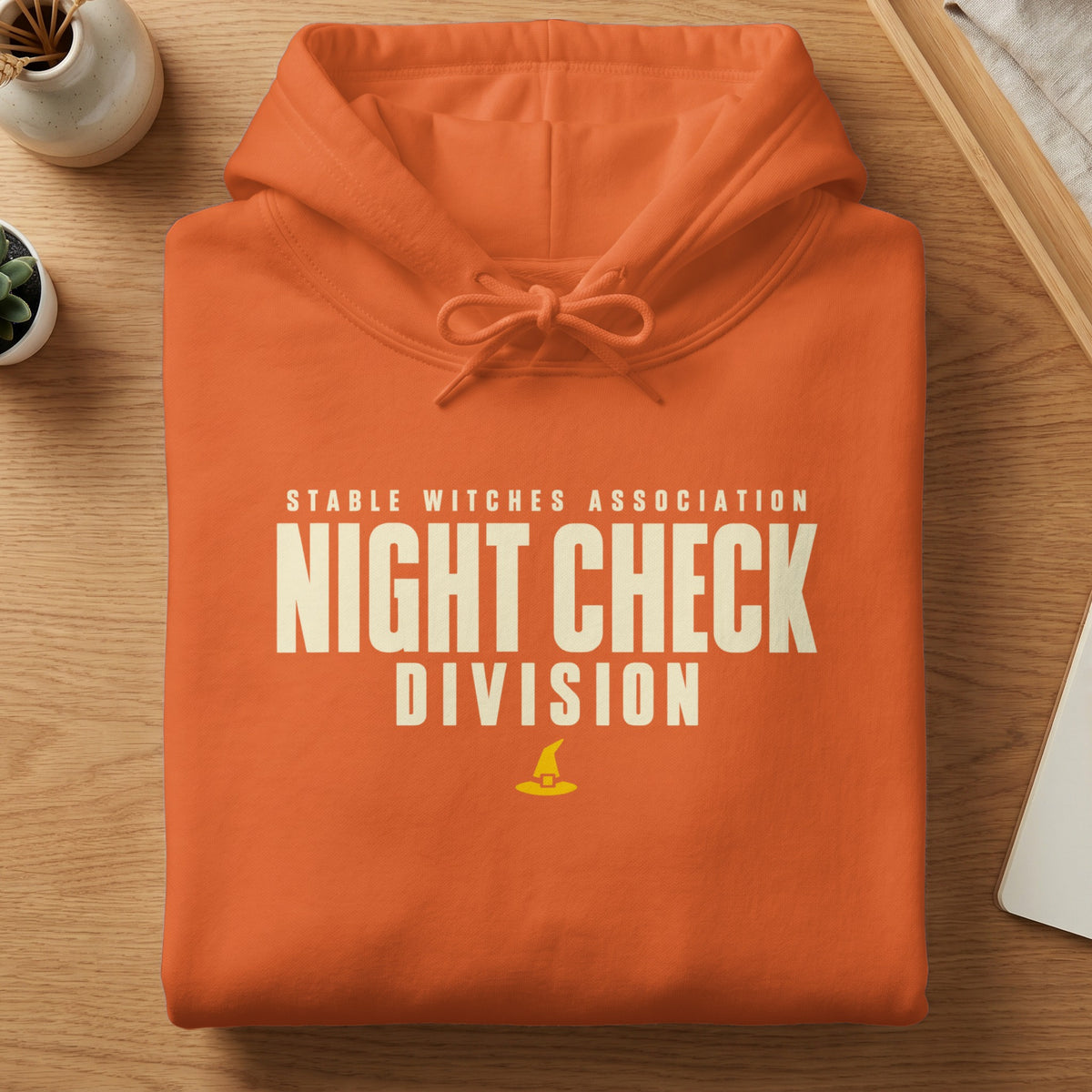 Orange hoodie with text "STABLE WITCHES ASSOCIATION NIGHT CHECK DIVISION" and a witch hat graphic.