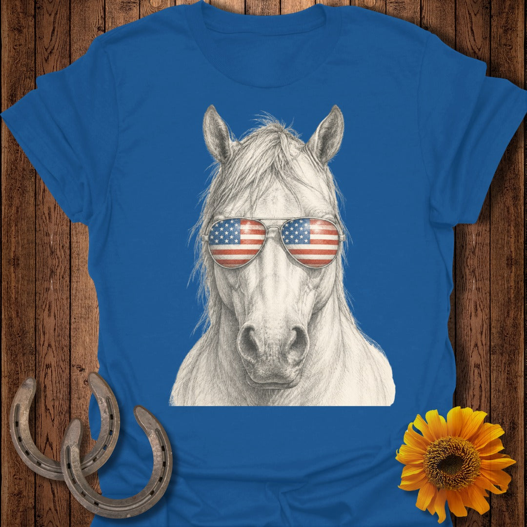 White horse wearing American flag sunglasses on a blue t-shirt.