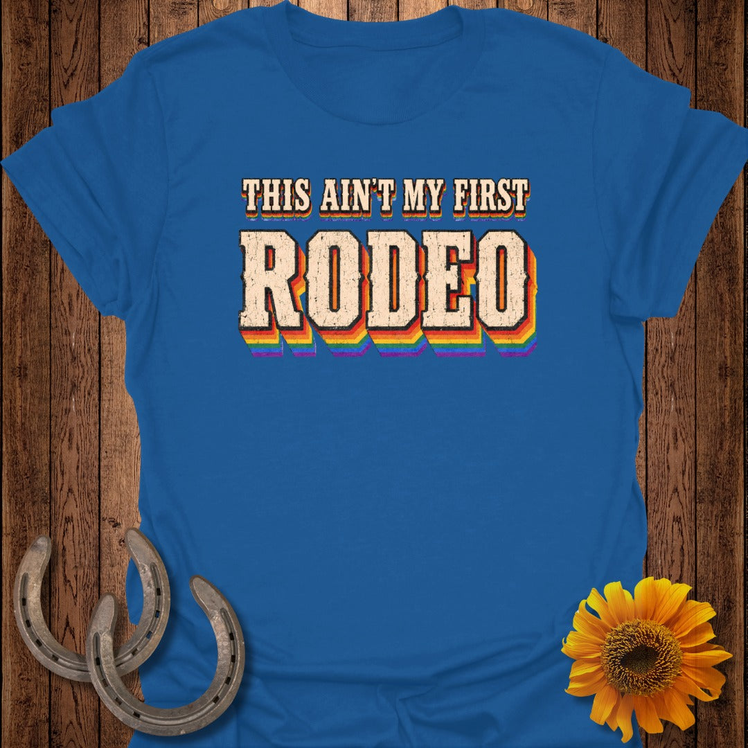 Blue t-shirt with "THIS AIN'T MY FIRST RODEO" in rainbow letters.