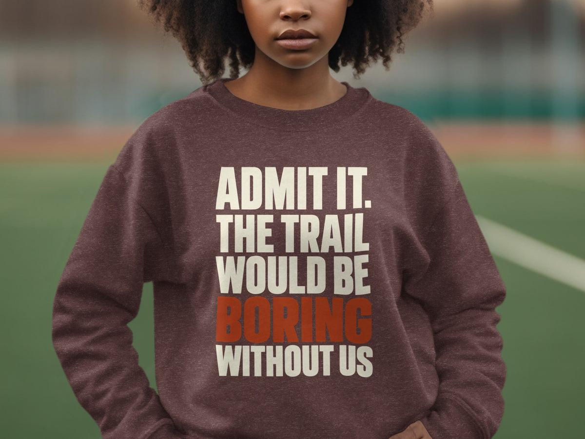 A person wears a brown sweatshirt printed with white and orange text reading, Admit it. The trail would be boring without us.