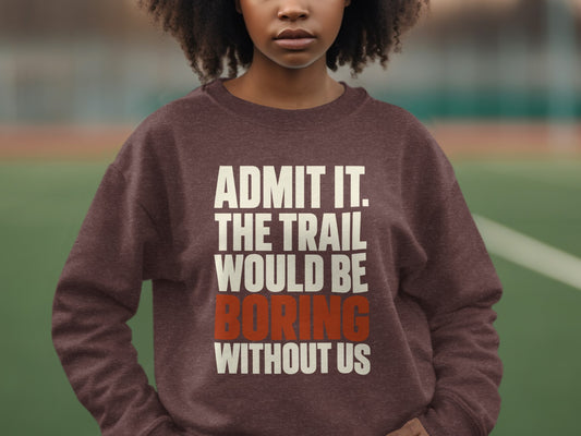 A person wears a brown sweatshirt printed with white and orange text reading, Admit it. The trail would be boring without us.