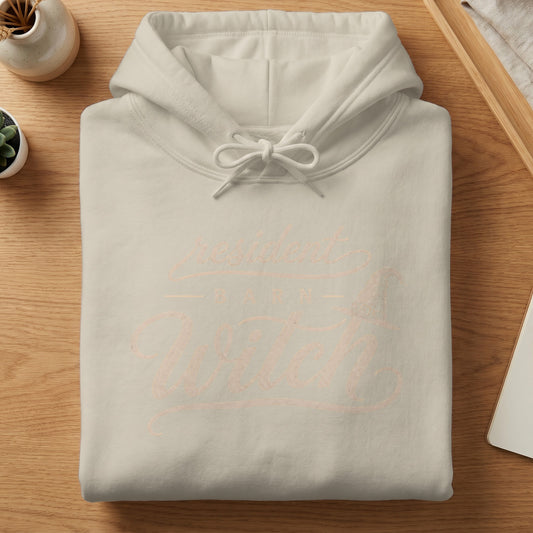 Light cream hoodie with "resident barn witch" text and witch hat graphic.