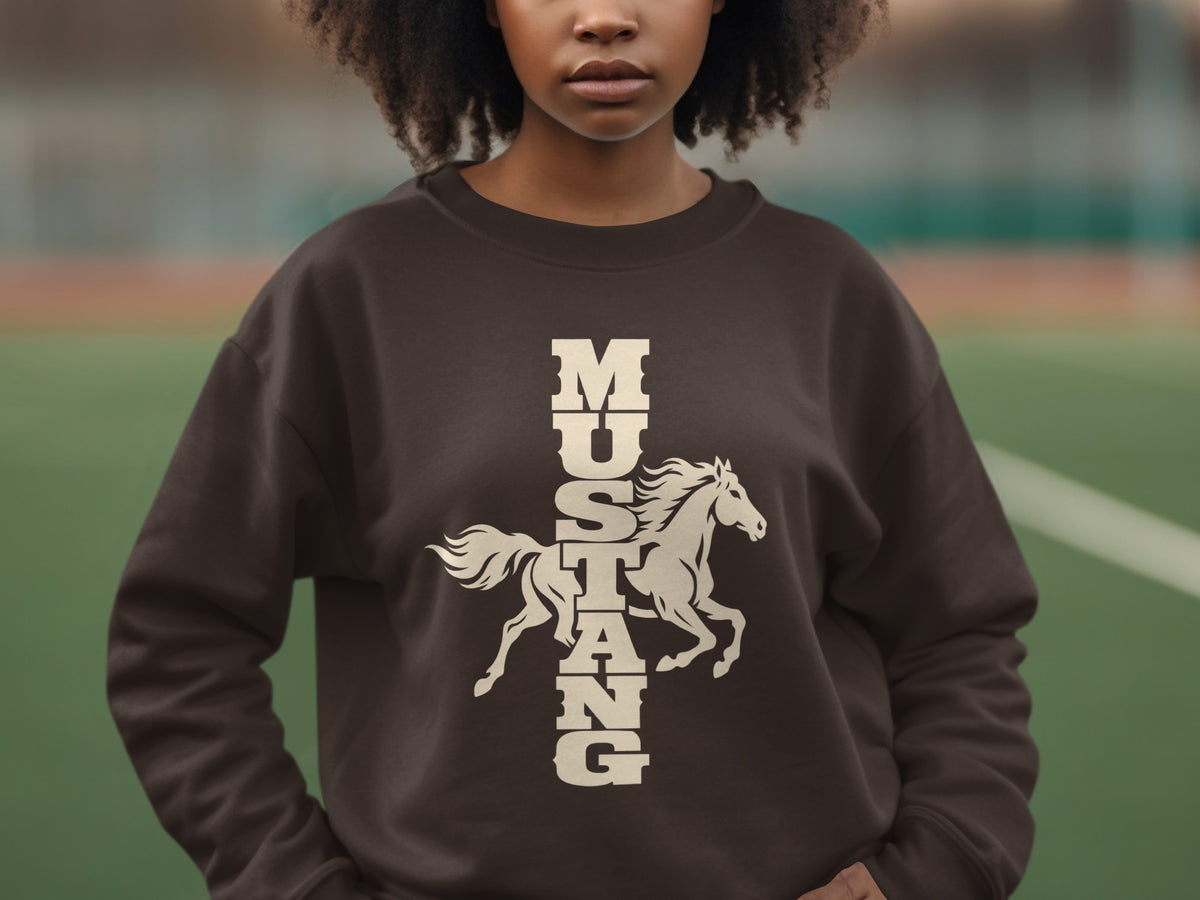 A person wears a dark brown crewneck sweatshirt featuring a cream graphic of a galloping horse and the vertical text MUSTANG.