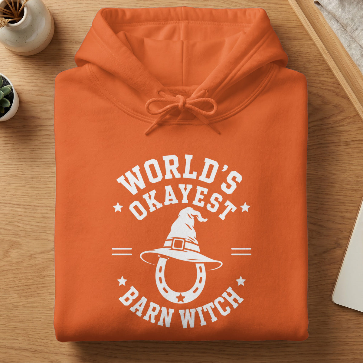 Orange hoodie with white graphic: "World's Okayest Barn Witch" and a witch hat over a horseshoe.