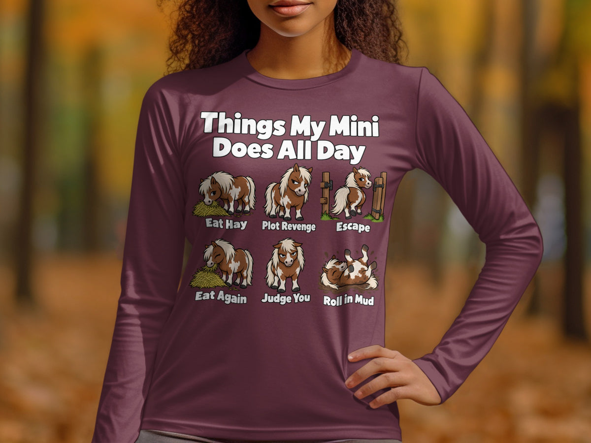A person wearing a maroon long-sleeve t-shirt featuring graphic illustrations and text about miniature horse behaviors.