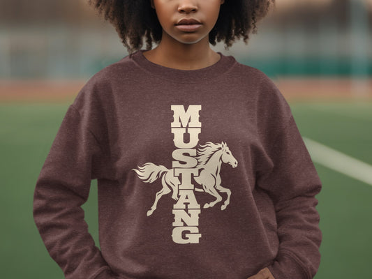 A person wearing a brown crewneck sweatshirt featuring a cream graphic of a running horse and vertical Mustang text.