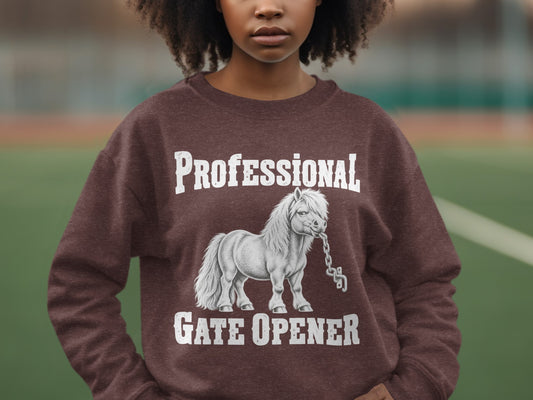 A person wearing a brown crewneck sweatshirt featuring a graphic of a pony holding a chain in its mouth, with text reading PROFESSIONAL GATE OPENER.