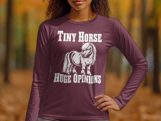 A person wearing a plum long-sleeve shirt with white text reading Tiny Horse Huge Opinions above and below a pony illustration.