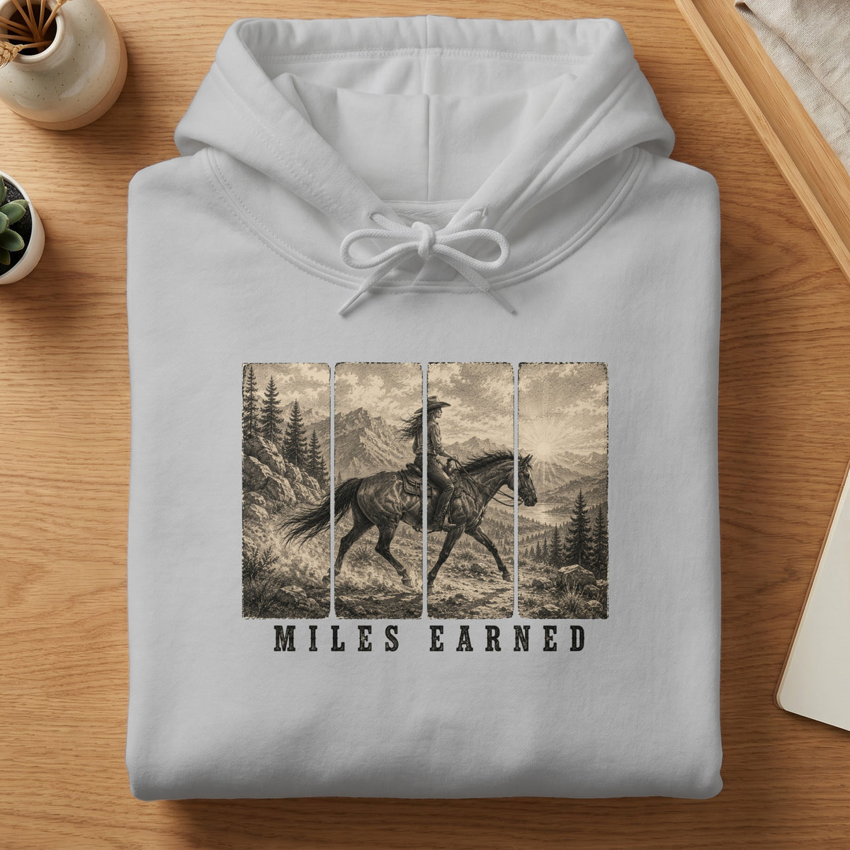 White hoodie with a vintage western graphic of a rider on horseback and text "MILES EARNED".